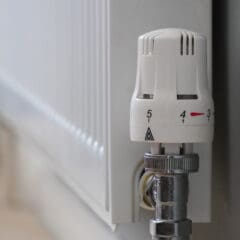 Close-up of a white radiator with a thermostatic valve, set between levels 3 and 4, mounted against a light-colored wall and floor.