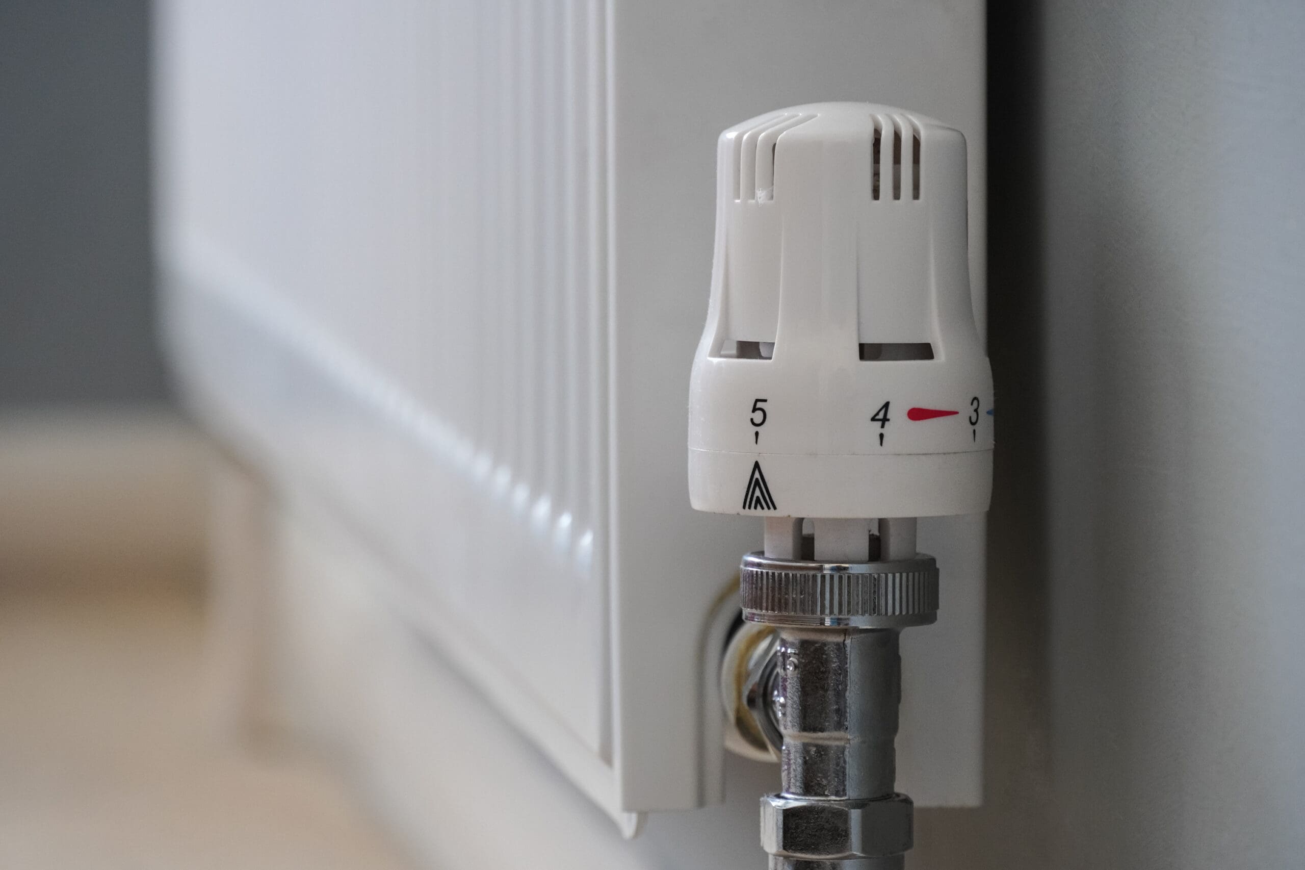 Close-up of a white radiator with a thermostatic valve, set between levels 3 and 4, mounted against a light-colored wall and floor.