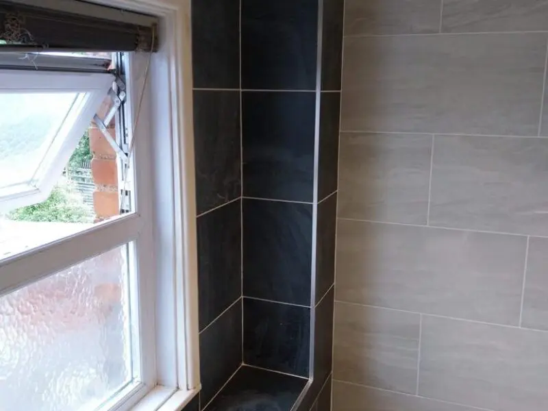 A bathroom with tiled walls showing a window that cannot fully open due to a tiled shelf or partition built closely next to it, blocking its movement.