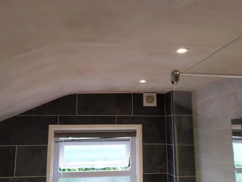 Bathroom with a sloped ceiling, recessed ceiling lights, a vent, a window with a blind, and tiled walls. A shower curtain rod is visible on the right side.